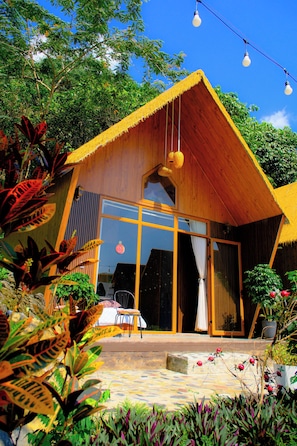 Une maison en bois avec de grandes fenêtres, un toit de chaume et une terrasse agrémentée de plantes.