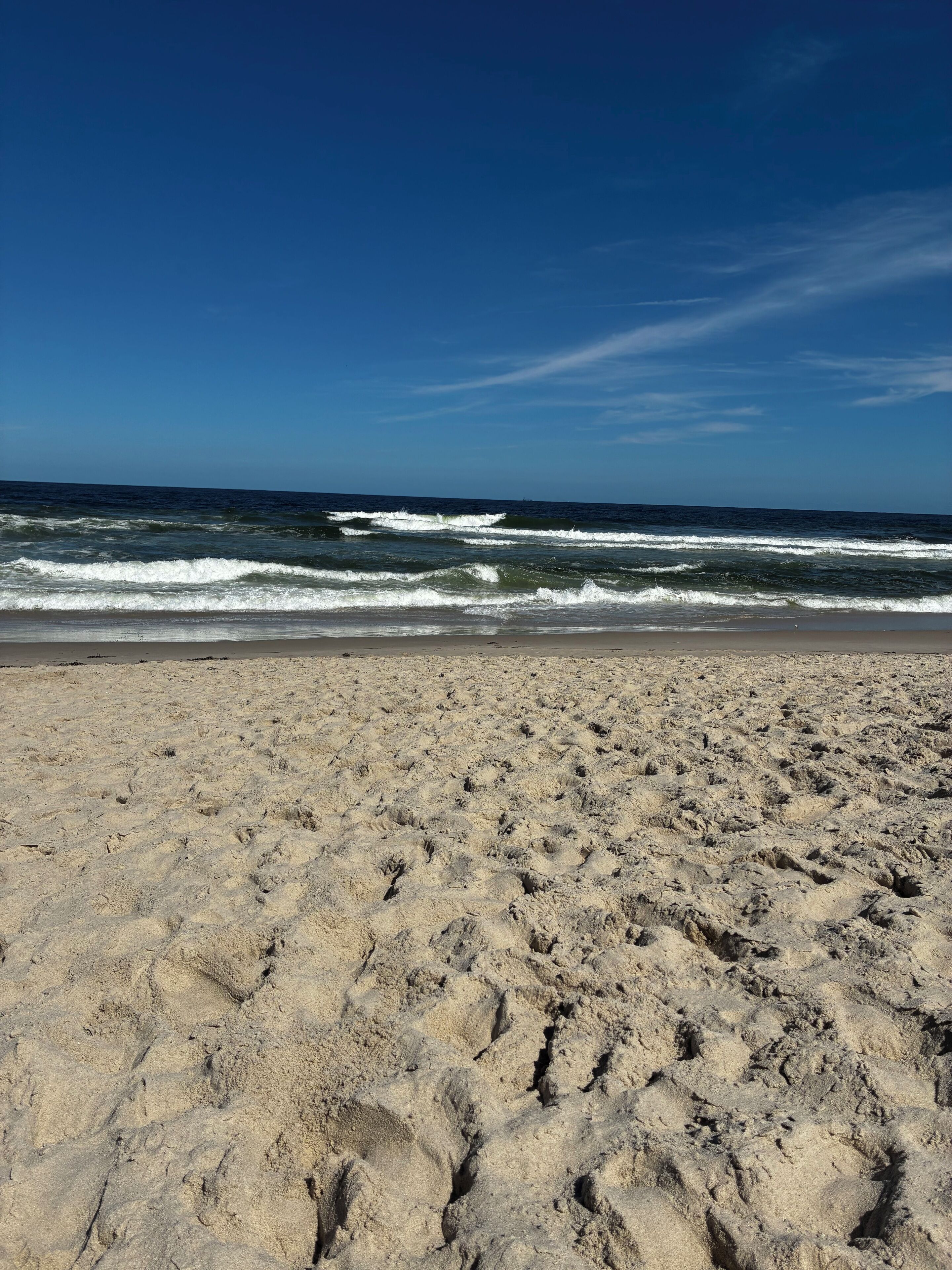 A sandy beach with footprints leading to the water, under a clear blue sky.