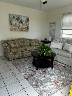 A living room with a patterned sofa, a round coffee table with a plant, a painting on the wall, and a motivational quote sign. - Lavallette 80s beach nostalgia (Lavallette)