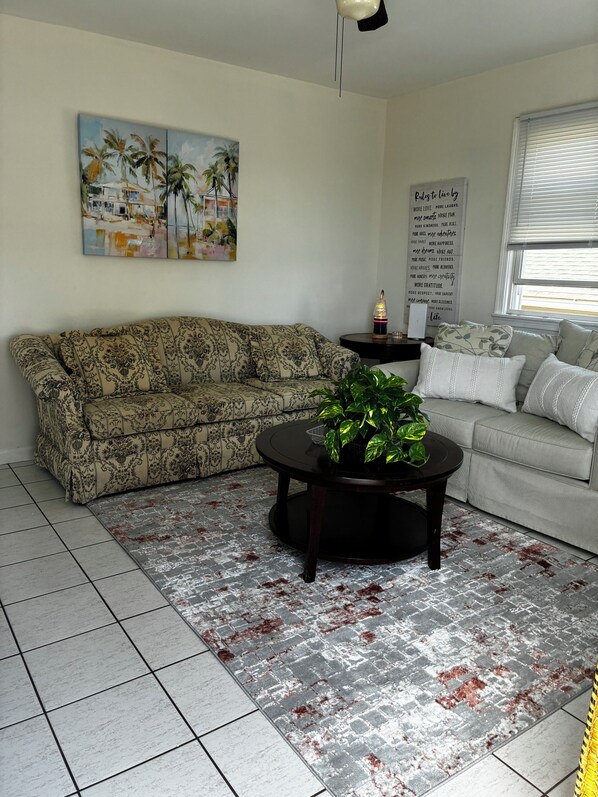 A living room with a patterned sofa, a round coffee table with a plant, a painting on the wall, and a motivational quote sign. - Lavallette 80s beach nostalgia (Lavallette)
