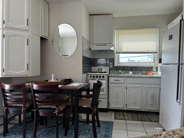 Una cocina con armarios blancos, una estufa, un fregadero y una zona de comedor con sillas y una mesa.