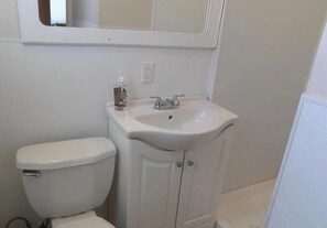 Ein Badezimmer mit einer weißen Toilette, einem Waschbecken mit Spiegel darüber und einer Handdesinfektionsmittel-Flasche auf dem Waschbecken.