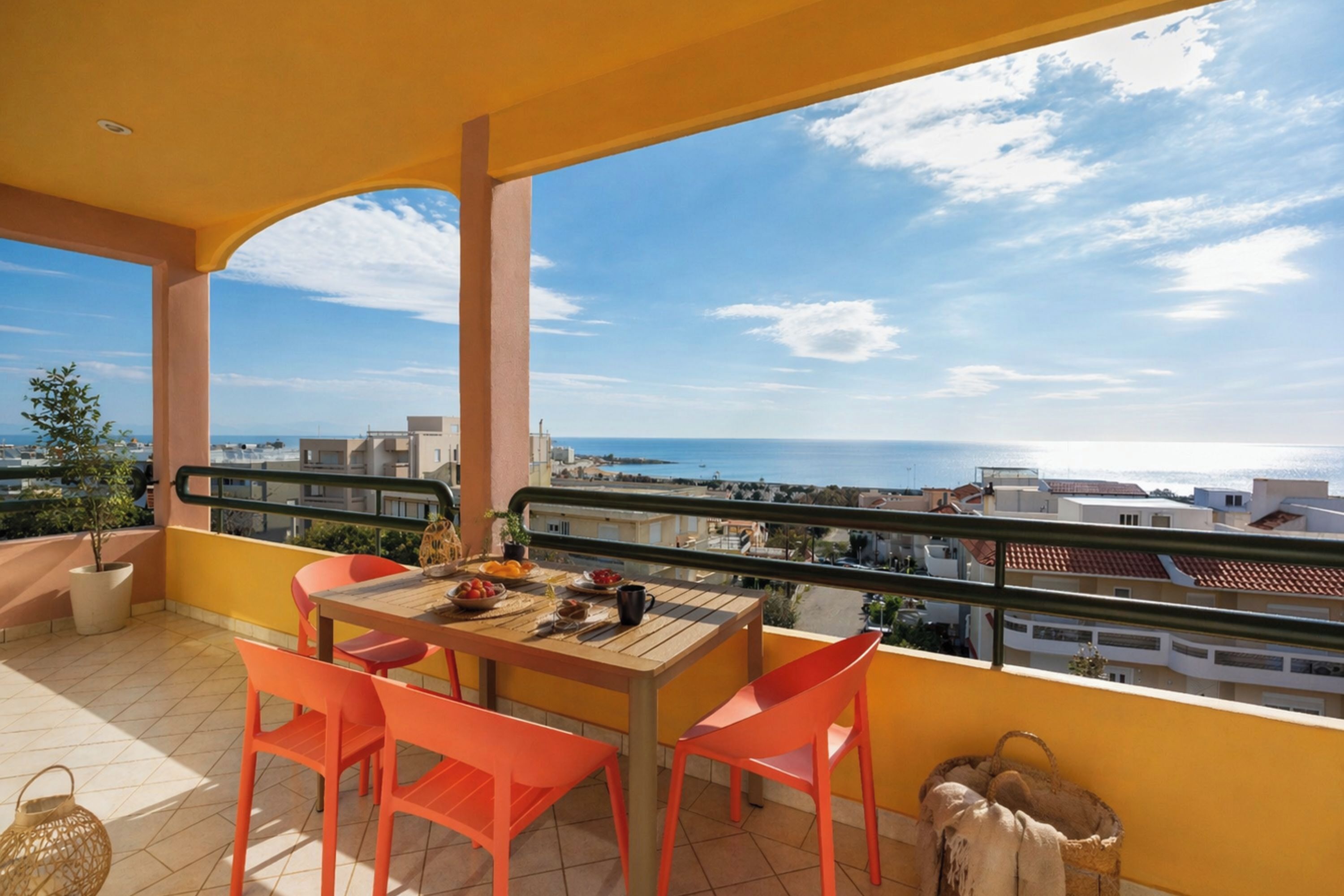 A balcony with a table and chairs, a view of the sea and buildings, and a railing.