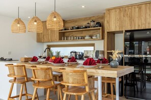 Una cocina moderna con armarios de madera, una isla central con taburetes y lámparas colgantes de mimbre, además de diversos electrodomésticos.