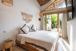 Un dormitorio con cama, cabecera de madera, un colgador de macramé y vistas a la vegetación exterior.