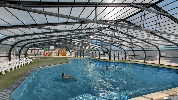 Una piscina interior amb un sostre de vidre, envoltada de gandules.