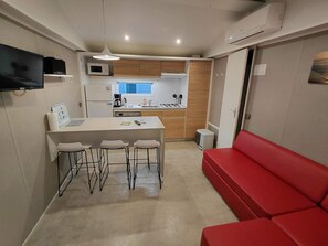 A compact kitchen with a dining area, a red sofa, and a TV mounted on the wall. - Air-conditioned mobile home with beach access, bed 160, 2 bathrooms, 2 WCs (Vendres)