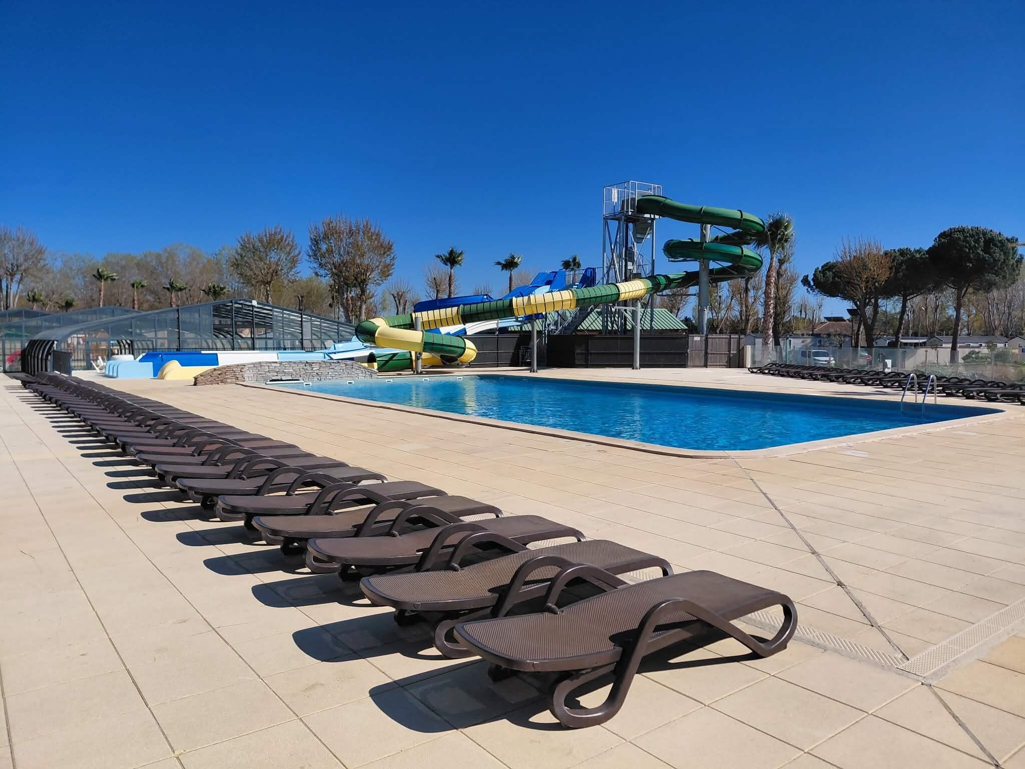 A pool area with lounge chairs, a water slide, and a clear blue sky.