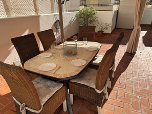 Un patio con una mesa lista para cuatro personas, rodeado de sillas de mimbre, una planta en maceta y una cesta.