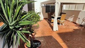 Un espace patio agrémenté de plantes en pot, de meubles en osier et d’un sol carrelé.