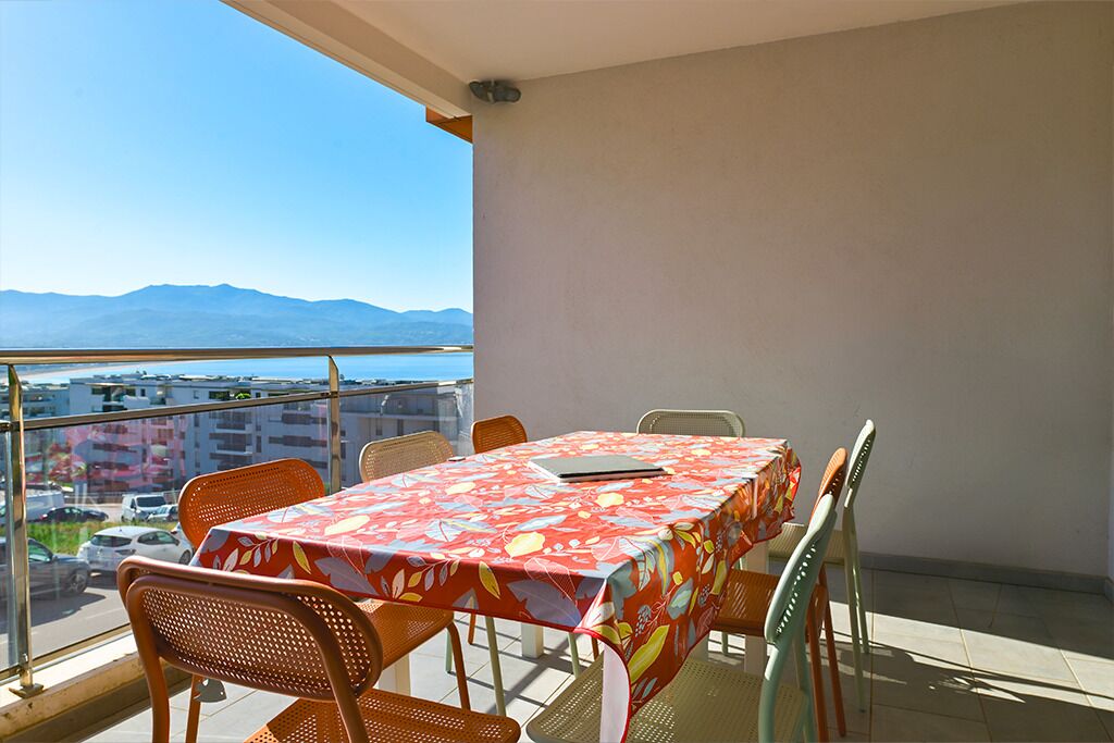 A balcony with a table and chairs, a clear view of the city and mountains.