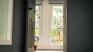 Pasillo que conduce a una habitación con una puerta, un ventanal y vistas al exterior con vegetación.