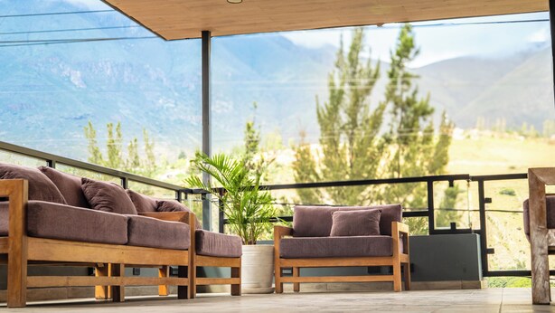 Un balcón con un sofá y un sillón de madera, una planta en maceta y vistas a montañas.