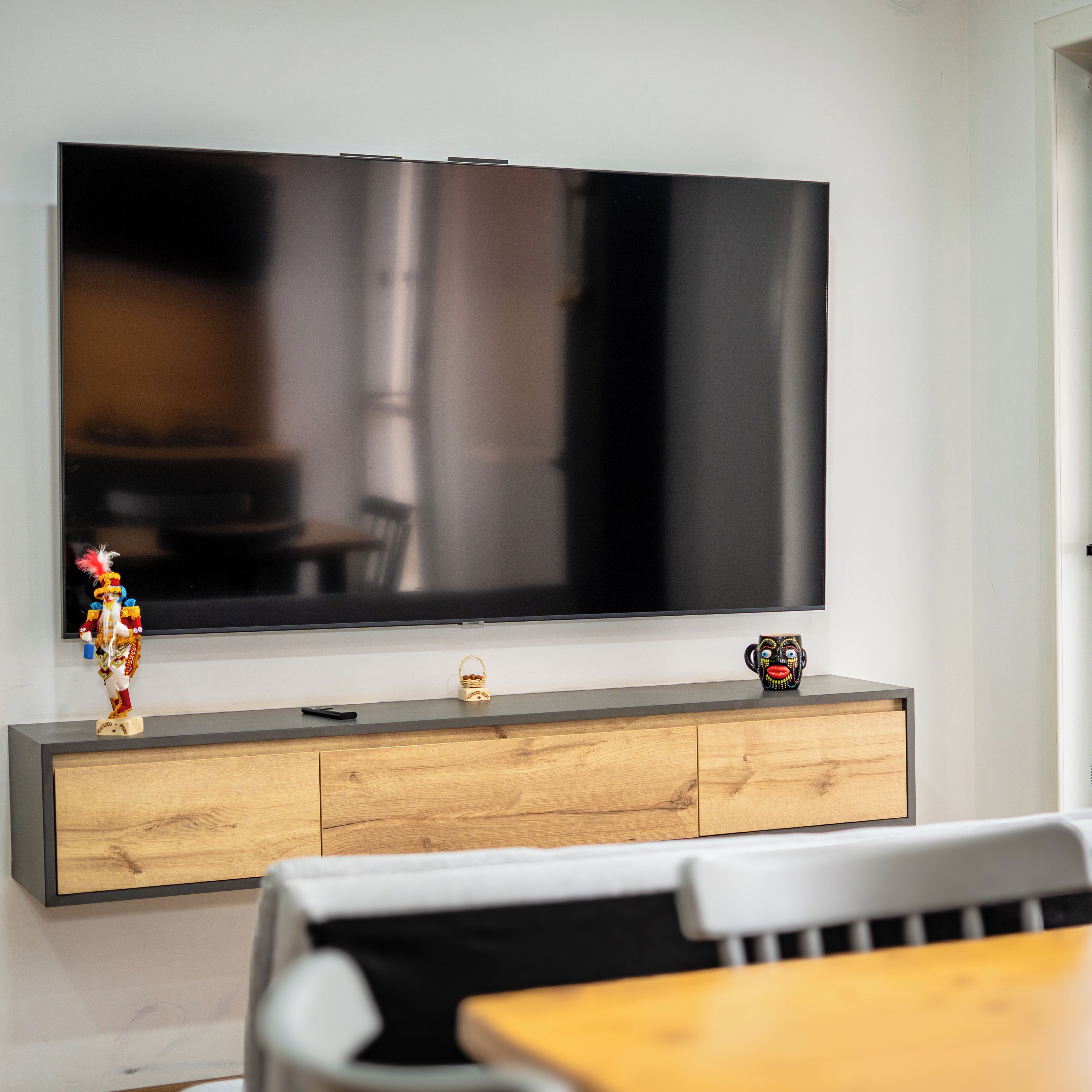 Un televisor de pantalla plana montado en la pared, sobre un mueble de madera con un control remoto y un pequeño adorno.