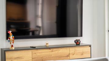 Un televisor de pantalla plana montado en la pared, sobre un mueble de madera con un control remoto y un pequeño adorno.