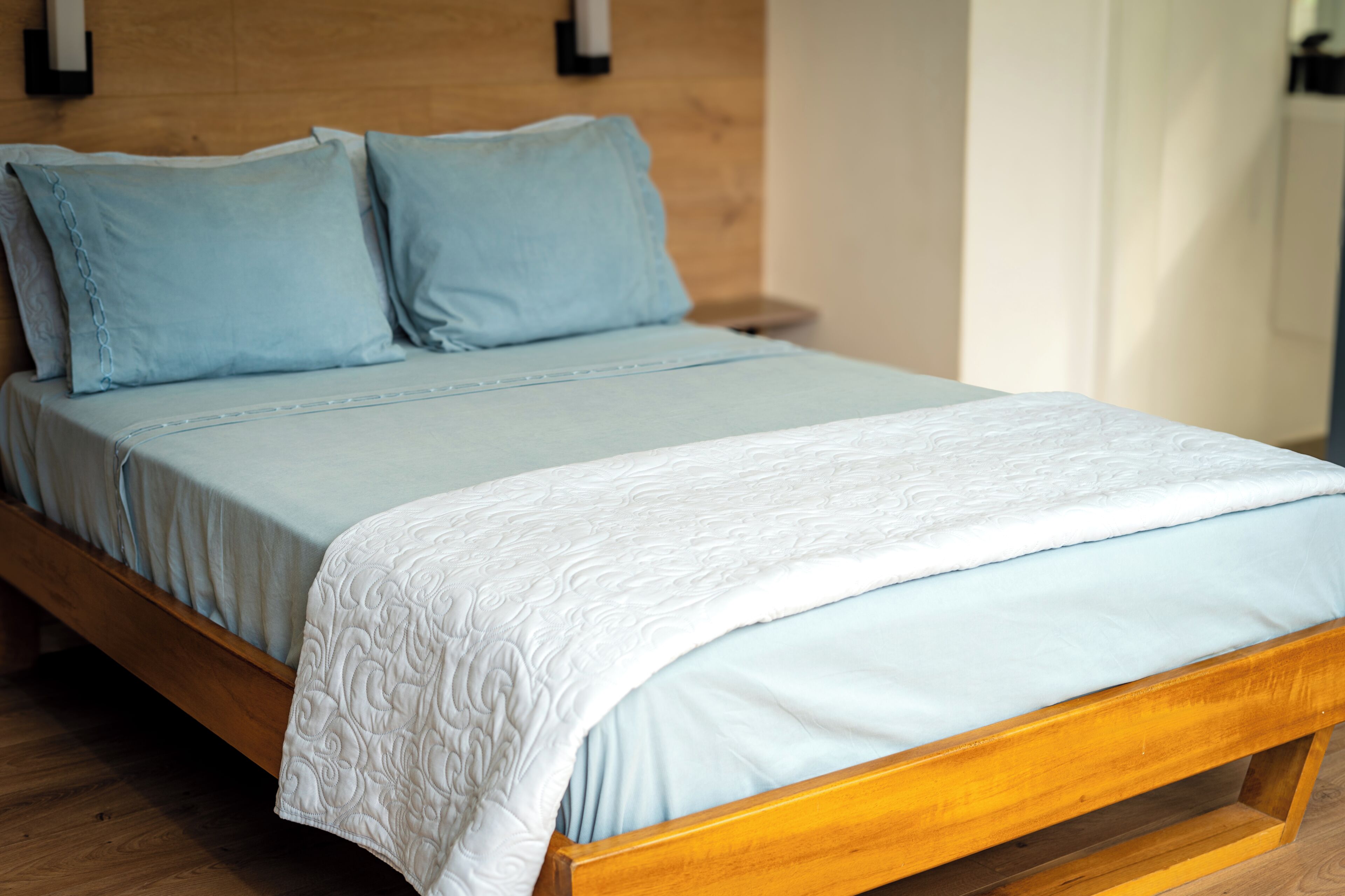 A bed with a wooden frame, a light blue mattress, and matching pillows.