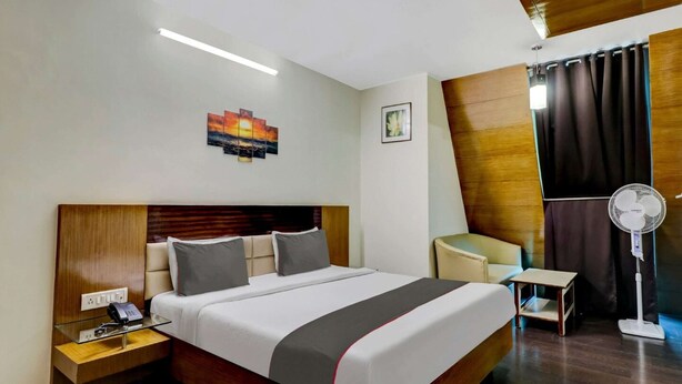 Habitación de hotel con una cama grande, mesita de noche con teléfono, escritorio con silla, ventilador de pie y obras de arte en las paredes.