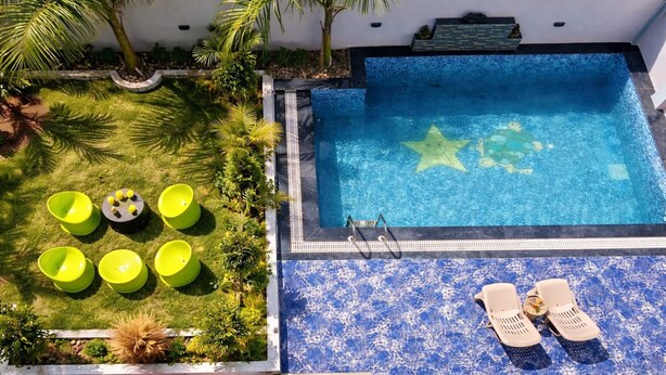 Una piscina en la azotea con suelo de mosaico azul, sillones reclinables verdes y una pequeña mesa con una flor.