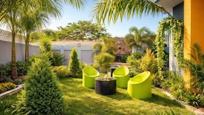 Un jardín con sillas verdes, una mesa redonda y diversas plantas.