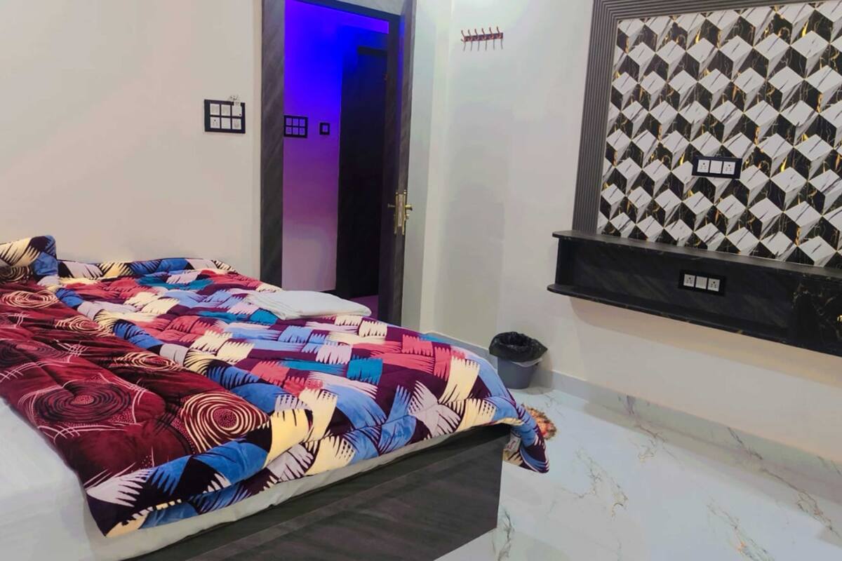 A bedroom with a bed, a door, a wall-mounted shelf, and a patterned wall.