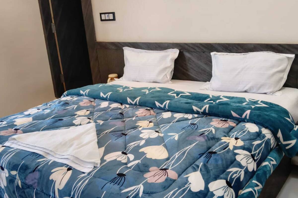 A bed with a floral duvet, a wooden headboard, and a dark wardrobe.