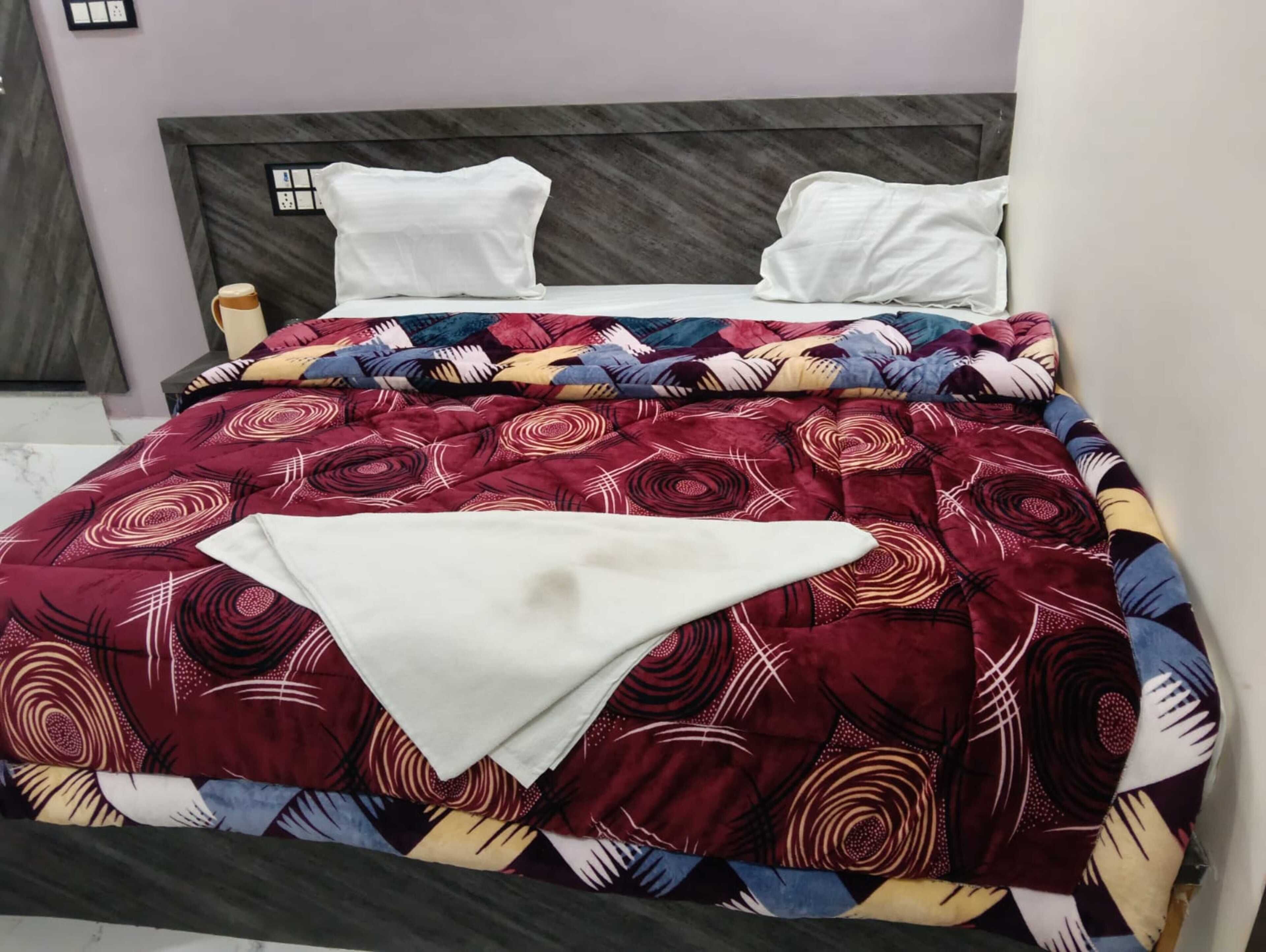 Un llit amb un estovat estampat, dos coixins i una taula de nit amb una làmpada.