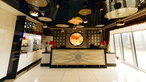 Un moderno vestíbulo de hotel con un mostrador de recepción, varias lámparas colgantes y un gran reloj de pared.