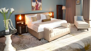 Habitación de hotel con una cama grande, mesitas de noche, una silla, un florero con flores y un cuadro en la pared.