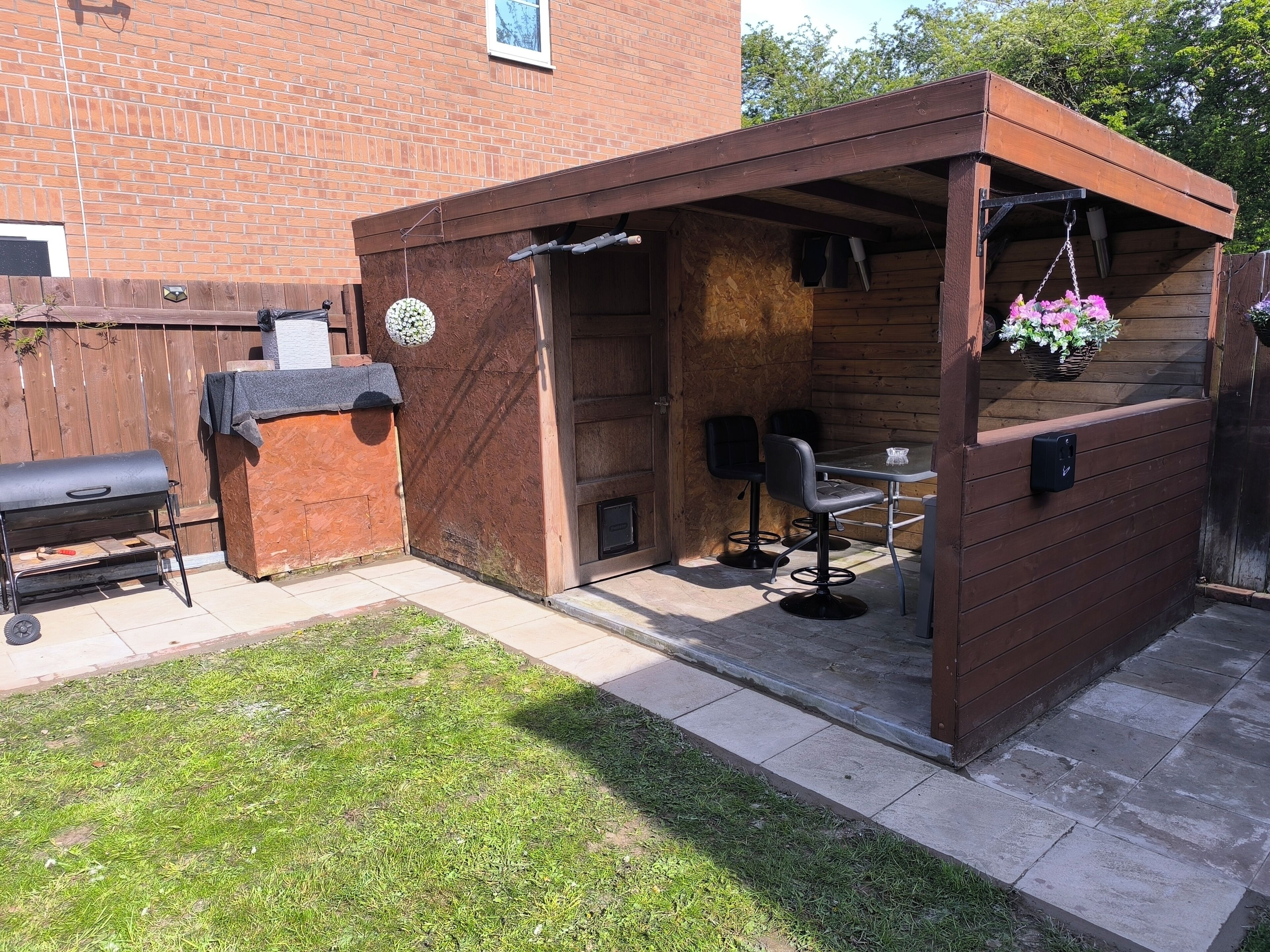 A wooden outdoor patio with a barbecue grill, two chairs, and a table.