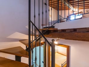 Eine mehrgeschossige Holztreppe mit Metallgeländern und Blick in einen anliegenden Raum.
