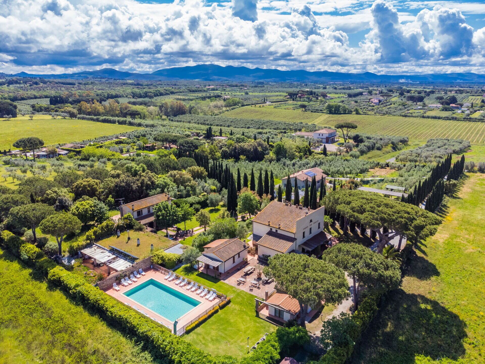 Luftaufnahme eines Landguts mit Schwimmbad, mehreren Gebäuden und umliegender Grünfläche.