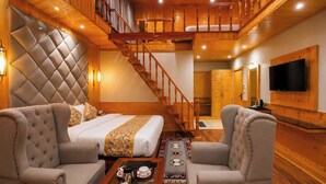 Ein Hotelzimmer mit einem Bett, zwei Sesseln, einem Couchtisch, einem Fernseher, einer Treppe und Holzwandverkleidung.