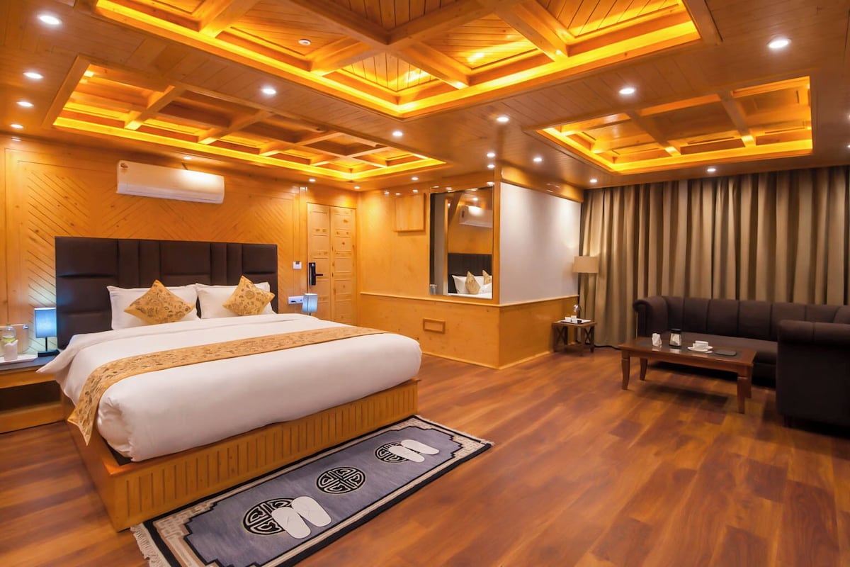 Habitación de hotel con una cama grande, un sofá, un espejo, techo de madera y suelo de madera.