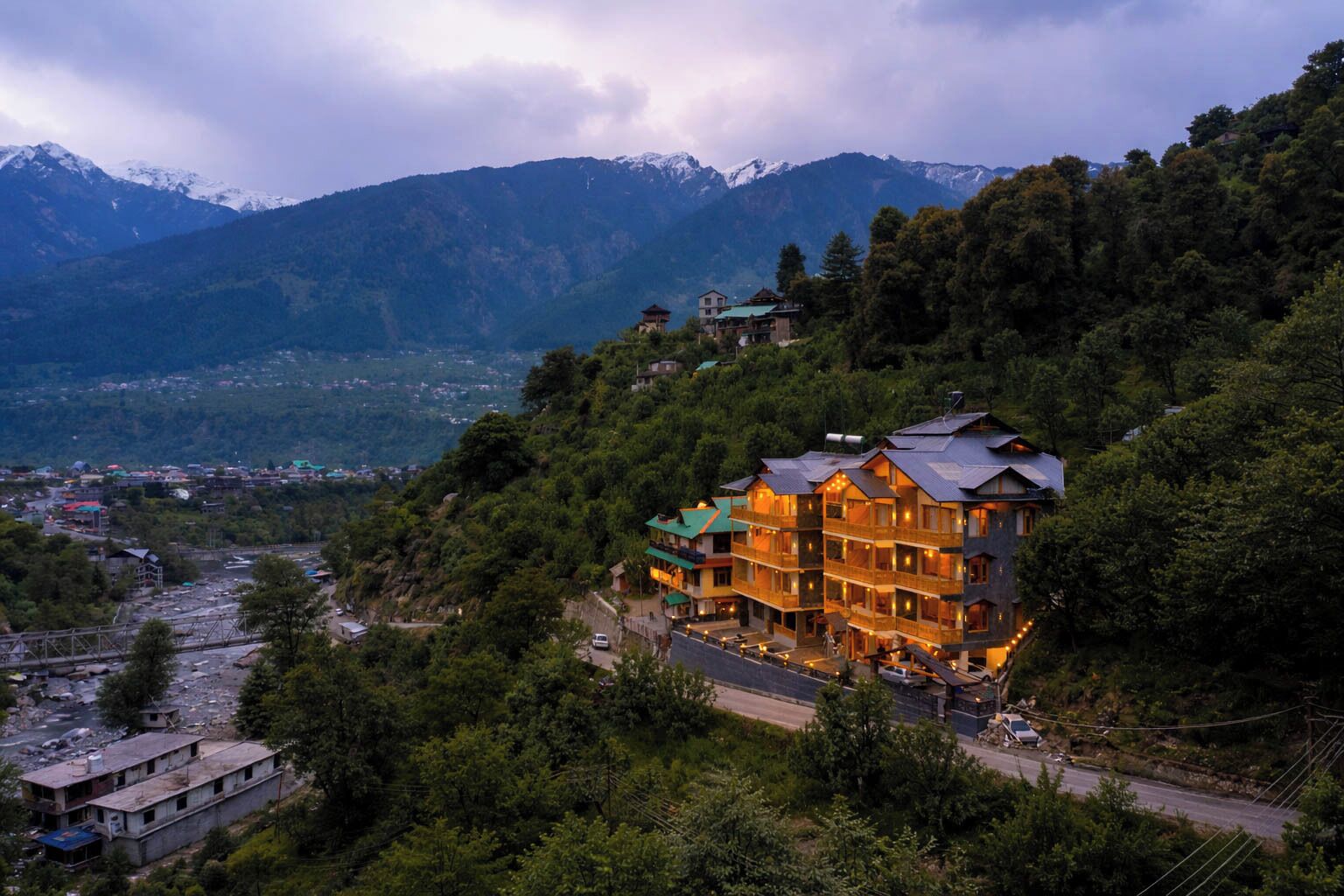 Un hotel de varios pisos con un estilo arquitectónico tradicional, rodeado de vegetación exuberante y montañas al fondo.