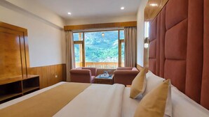 Ein Hotelzimmer mit einem großen Bett, einer Sitzecke mit Tisch und Blick auf eine gebirgige Landschaft.