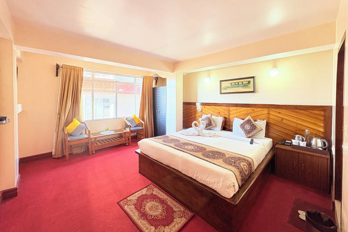 Habitación de hotel con una cama grande, un escritorio con silla, una ventana con cortinas y una lámpara fijada a la pared.