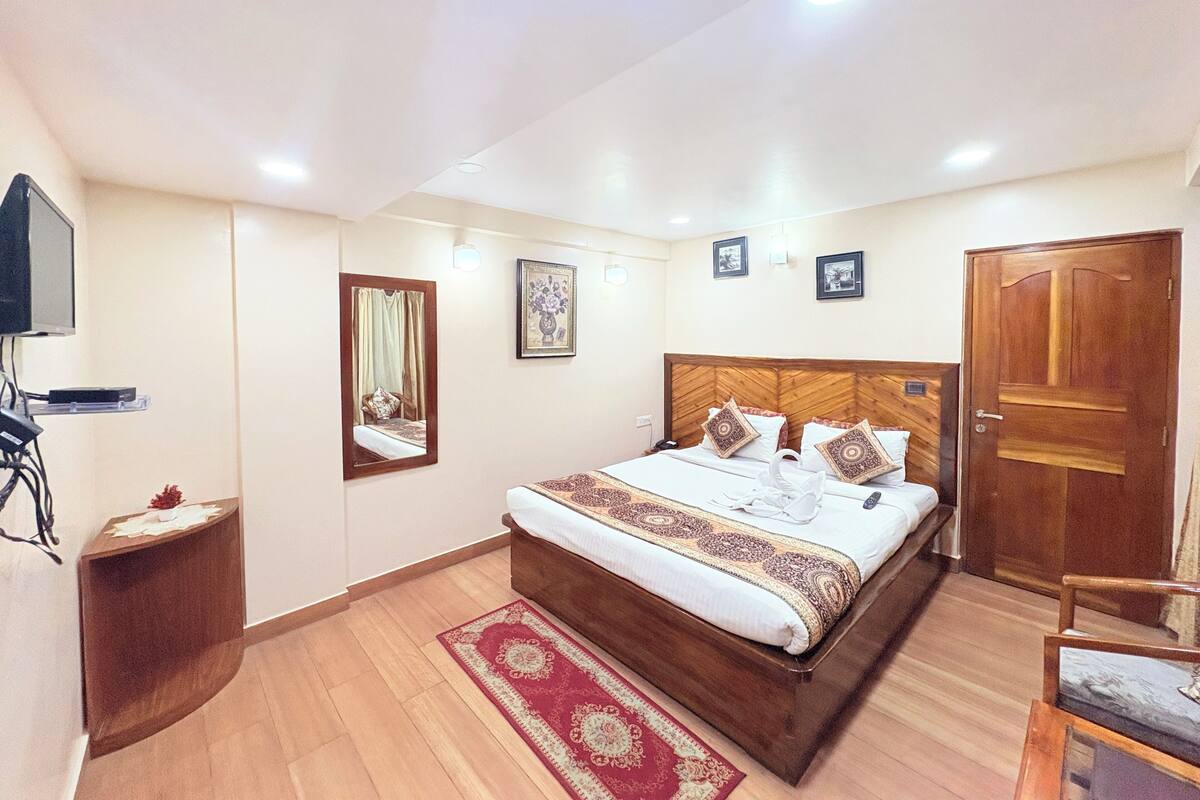 Una habitación de hotel con una cama, cabecera de madera, espejo, televisor y una puerta.