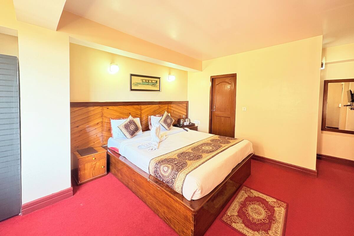 Un dormitorio con cabecera de madera, una cama con almohadas y una colcha, una mesita de noche, una puerta de madera y una alfombra roja.