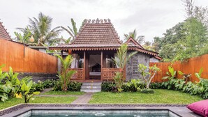 Ein traditionelles Holzhaus mit Ziegeldach, einer kleinen Veranda und einem Swimmingpool im Vordergrund.