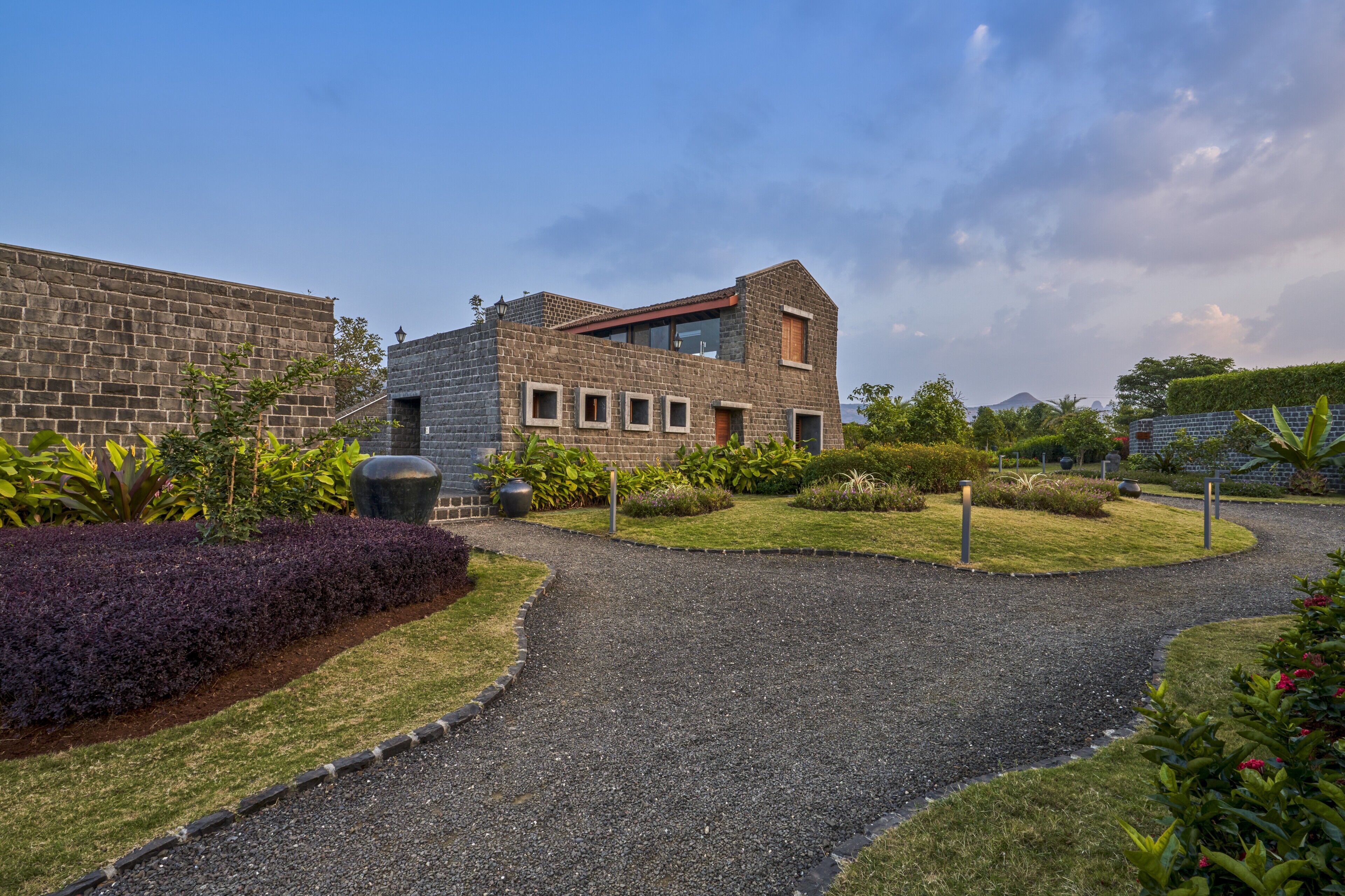 A modern building with a brick facade, a gravel pathway, and landscaped gardens.
