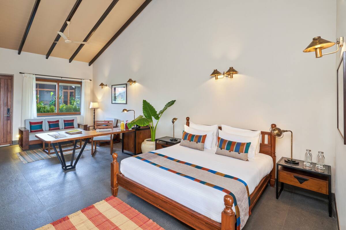 A bedroom with a bed, bedside tables, a desk, a chair, a window with curtains, and wall-mounted lamps.