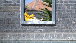 Un ventanal con el reflejo de una persona vestida de amarillo, un muro de ladrillo y un cielo despejado.
