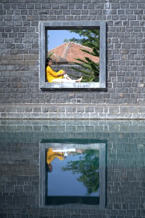 A window with a reflection of a person in a yellow outfit, a brick wall, and a clear sky. - Viveda Wellness Resort (Trimbak)