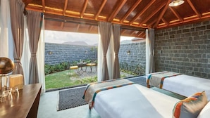 Una habitación con dos camas, una mesa y vistas a un jardín y montañas.