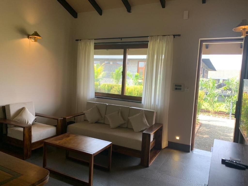 A room with a sofa, two chairs, a coffee table, a window with curtains, and a door leading outside.