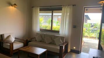 A room with a sofa, two chairs, a coffee table, a window with curtains, and a door leading outside.