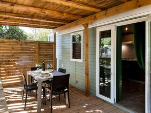 Eine überdachte Terrasse mit Tisch und Stühlen, ein Holzboden und eine Glastür zum Küchenbereich.