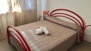 Un lit simple avec un cadre en métal rouge, une couvre-lit beige à motifs et une serviette blanche posée sur le lit.