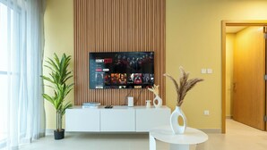 A modern living room with a flat-screen TV mounted on a wall, a white console table, a potted plant, and a decorative vase with pampas grass. - Downtown Dubai - Pool & Gym Access (Dubai)