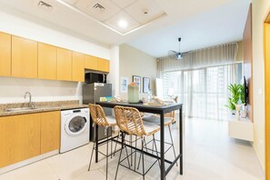 A modern kitchen with wooden cabinets, a washing machine, and a dining area with wicker chairs. - Downtown Dubai - Pool & Gym Access (Dubai)